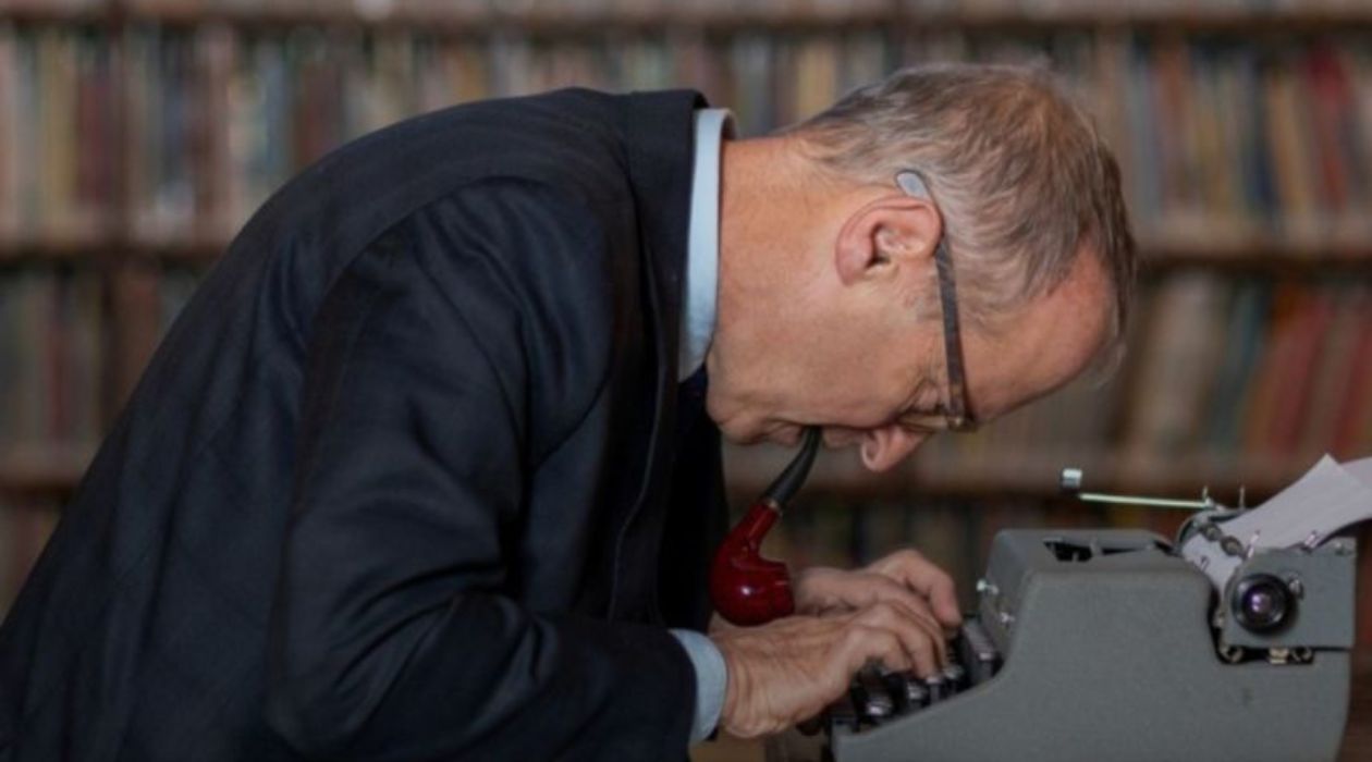 David Sedaris hunched over a typewriter with a pipe in his mouth